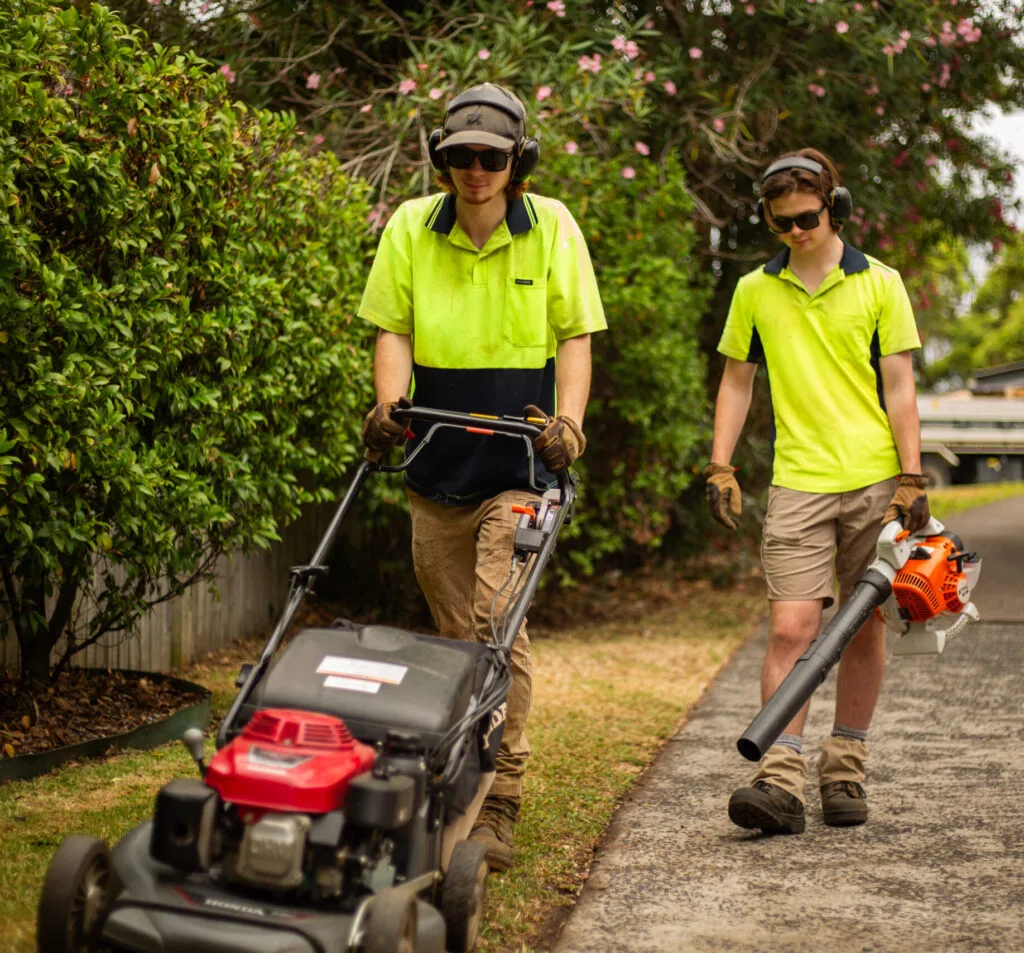 The Young Brothers walk down the pavement with a lawn mower and a leaf blower